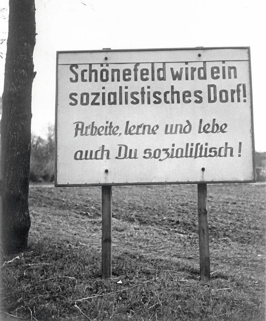 Ein_Schild_im_Kreis_Zossen_mit_der_Aufschrift:_"Schönefeld_wird_ein_sozialistisches_Dorf!_Arbeite,_lerne_und_lebe_auch_D
